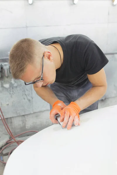 cute guy in black glasses with orange gloves displays the shape of the hood for the subsequent painting of the car. guy - a house painter working on a car in the garage