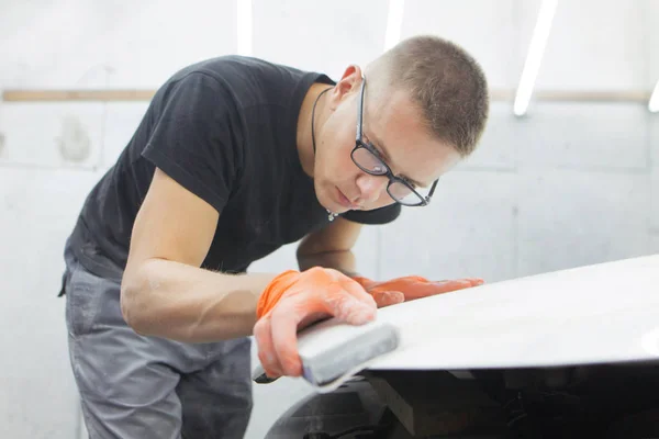 cute guy in black glasses with orange gloves displays the shape of the hood for the subsequent painting of the car. guy - a house painter working on a car in the garage
