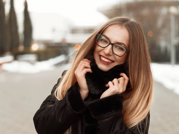 siyah gözlüklü güzel sarışın gülümseyen kız kış şehirde yürür ve biraz donuyor