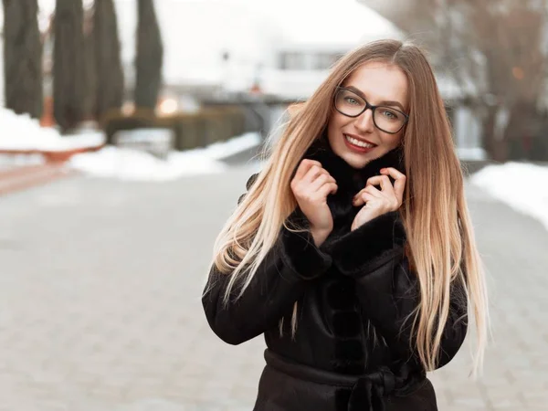 siyah gözlüklü güzel sarışın gülümseyen kız kış şehirde yürür ve biraz donuyor
