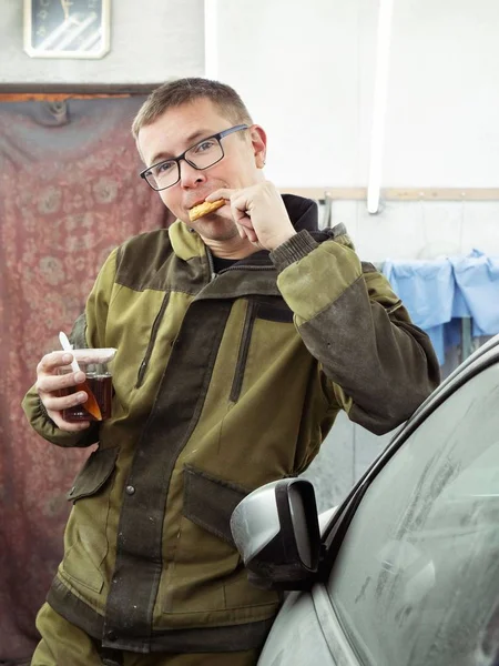 Cute guy in black glasses with black gloves displays the shape of the hood for the subsequent painting of the car. guy - a house painter working on a car in the garage