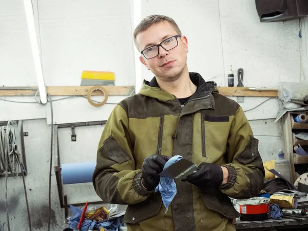 Cute guy in black glasses with black gloves displays the shape of the hood for the subsequent painting of the car. guy - a house painter working on a car in the garage