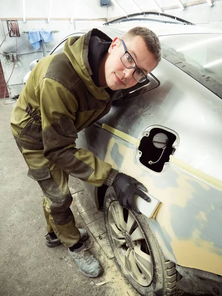 Cute guy in black glasses with black gloves displays the shape of the hood for the subsequent painting of the car. guy - a house painter working on a car in the garage