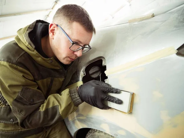 Cute guy in black glasses with black gloves displays the shape of the hood for the subsequent painting of the car. guy - a house painter working on a car in the garage