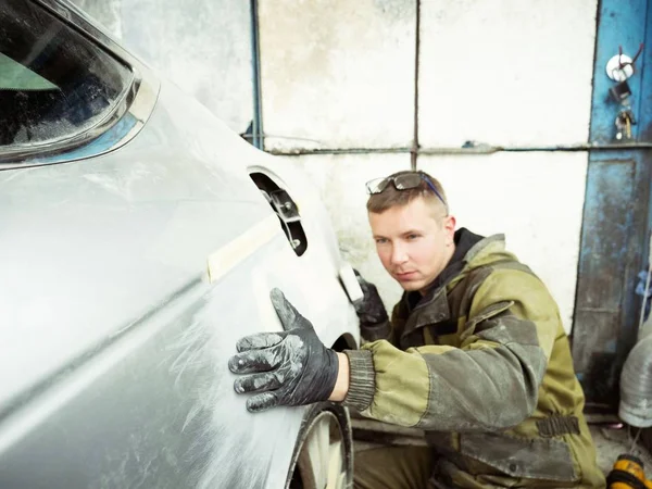 Cute guy in black glasses with black gloves displays the shape of the hood for the subsequent painting of the car. guy - a house painter working on a car in the garage