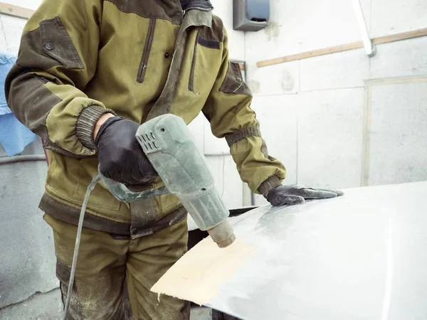 Cute guy in black glasses with black gloves displays the shape of the hood for the subsequent painting of the car. guy - a house painter working on a car in the garage