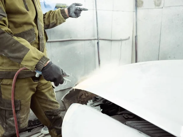 Cute guy in black glasses with black gloves displays the shape of the hood for the subsequent painting of the car. guy - a house painter working on a car in the garage