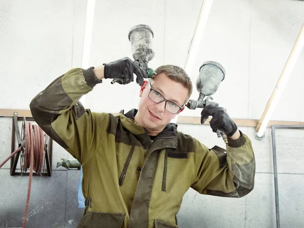 Cute guy in black glasses with black gloves displays the shape of the hood for the subsequent painting of the car. guy - a house painter working on a car in the garage