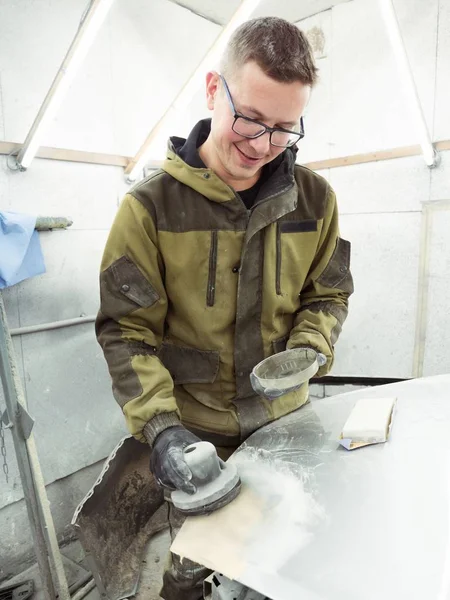 Cute guy in black glasses with black gloves displays the shape of the hood for the subsequent painting of the car. guy - a house painter working on a car in the garage