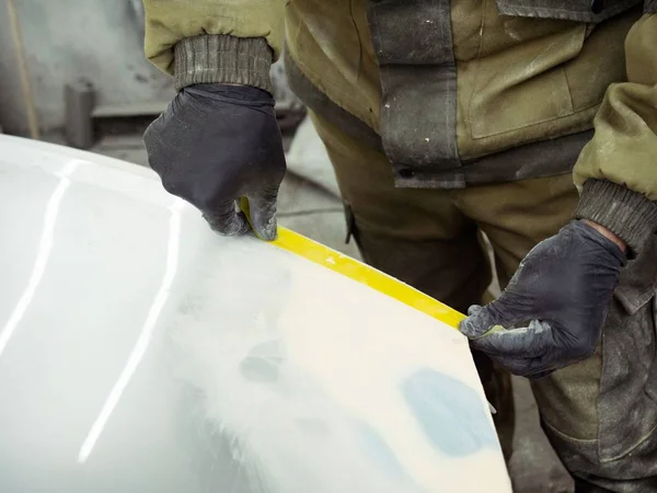 Cute guy in black glasses with black gloves displays the shape of the hood for the subsequent painting of the car. guy - a house painter working on a car in the garage