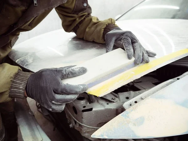 cute guy in black glasses with gloves displays the shape of the hood for the subsequent painting of the car. guy - a house painter working on a car in the garage