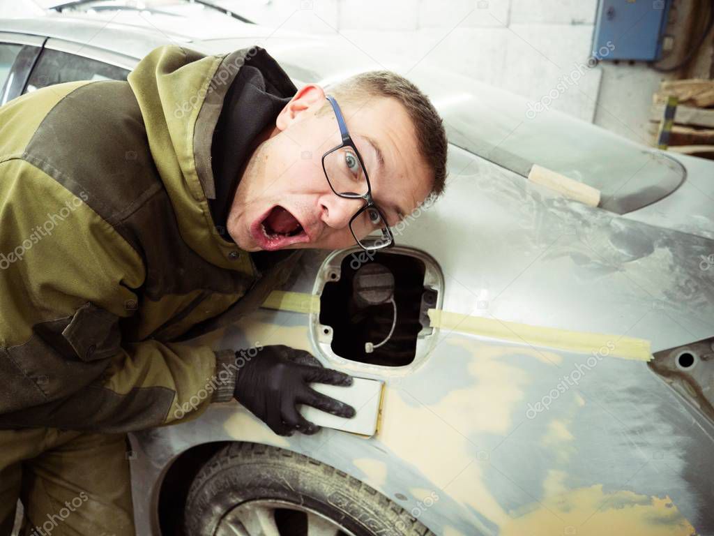 Cute guy in black glasses with black gloves displays the shape of the hood for the subsequent painting of the car. guy - a house painter working on a car in the garage