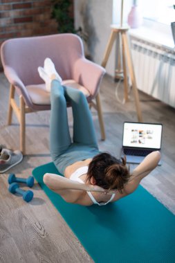 Genç, spor düşkünü kadının internetteki spor eğitmeni modern laptop ekranı var. Sağlıklı yaşam tarzı konsepti, online fitness ve spor dersleri. Pompalama presi