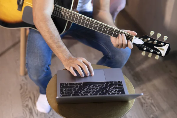 Genç bir adam koltukta bir odada oturur, online gitar çalmayı öğrenir. Çevrimiçi eğitim, çevrimiçi müzik dersleri, online vokal ve gitar eğitimi. Evde kal..