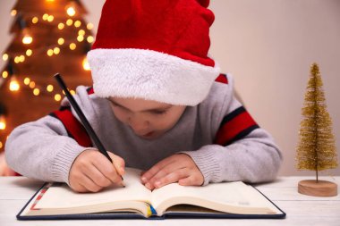 Noel çocuk yazmak mektup Noel Baba, çocuk, Santa şapka yazma istek listesi, odaklanmamış arka plan ışıklar.