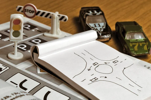 Not defteri, trafik kuralları kitabı, oyuncak arabalar, trafik ışıkları ve masa üzerindeki dur tabelası. Ehliyet sınavına çalışmak ve hazırlanmak