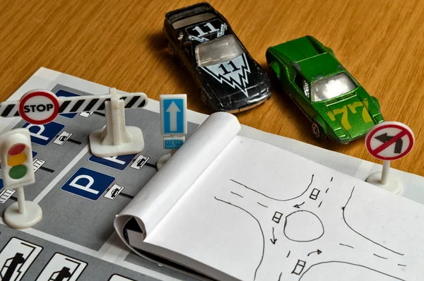 Not defteri, trafik kuralları kitabı, oyuncak arabalar, trafik ışıkları ve masa üzerindeki dur tabelası. Ehliyet sınavına çalışmak ve hazırlanmak