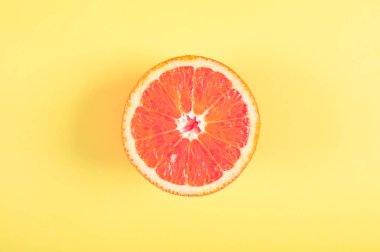 Sarı pastel renkli arka plan üzerinde yarım kanlı turuncu meyve üstten görünüm