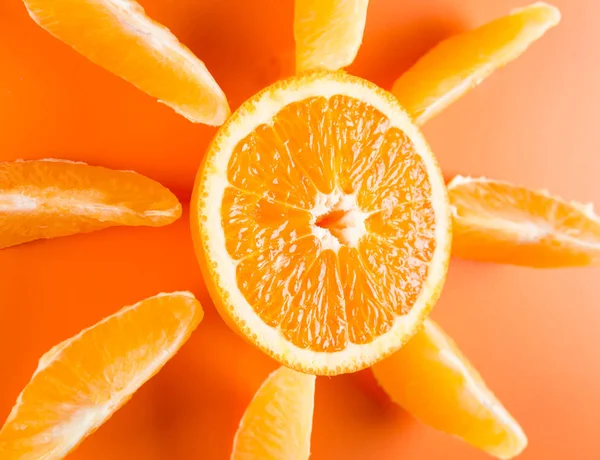 Orange slices spread around a cut half of an orange fruit on orange colored background