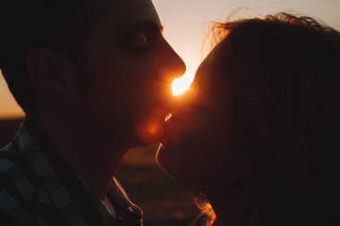Bir öpücük ve genç bir çift gün batımı ve aralarında parlıyor akşam güneşi karşı hassasiyet silüeti
