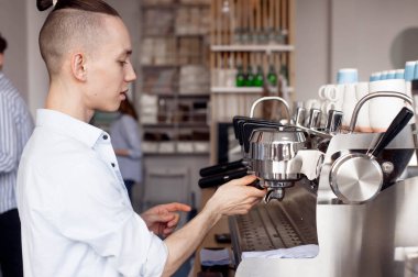 Şık bir saç modeli olan genç bir Barista adam bir kafede çalışıyor ve kahve makinesi filtre sahibinden unscrews