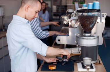 Genç bir adam bir Barista çalışır, o kahve makinesi standları ve filtre çekilmiş kahve ile doldurur.