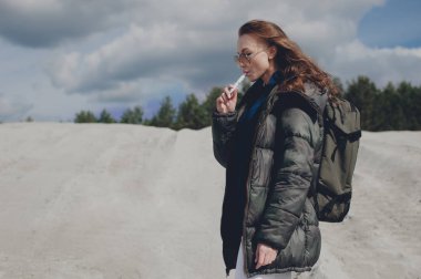 Bir dağ alan üzerinde duran ve elektronik sigara sigara güzel kız.