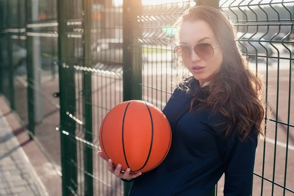 Bir yaz bahçesi, ayakta akşam ve bir basketbol topu tutan güzel kız. Metniniz için bir yer ile kameraya bakıyor