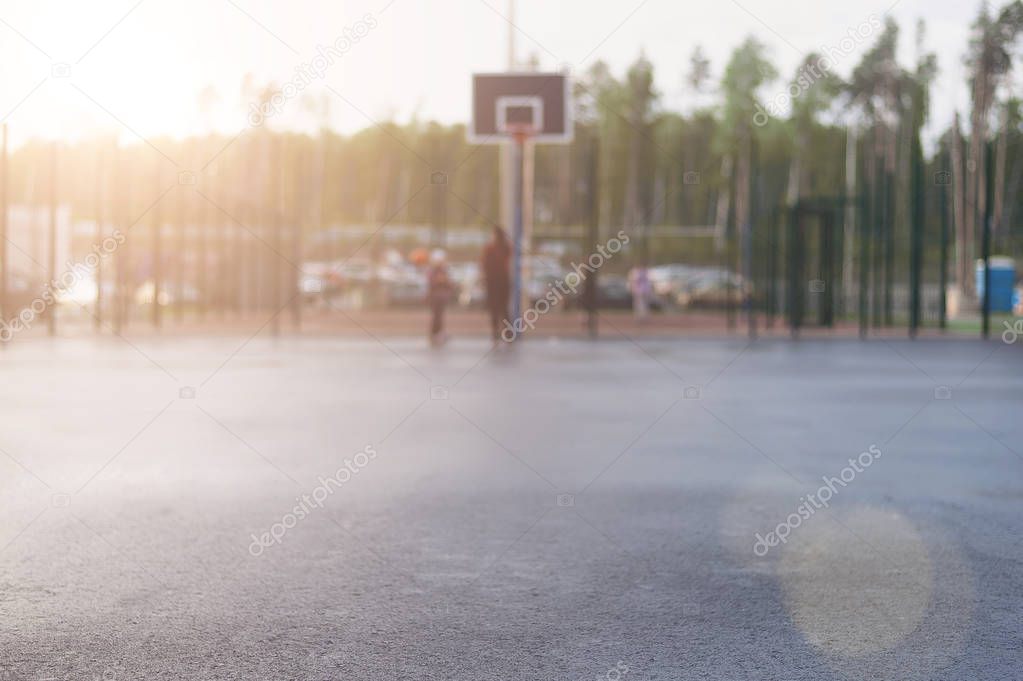Wet asphalt in focus for text on the background of street basketball court on which people play and which shines the evening sun