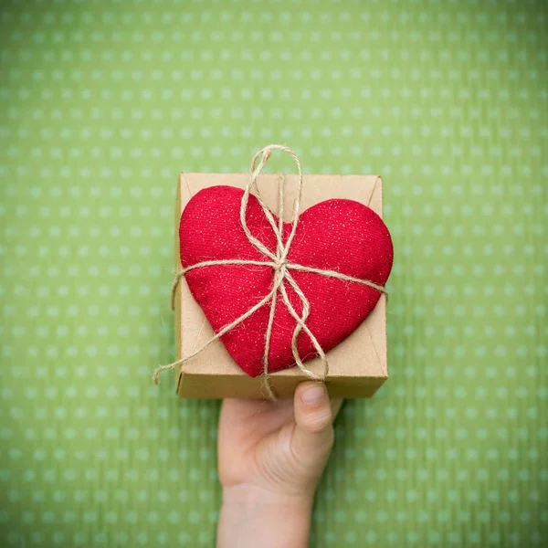Uma criança tem um coração vermelho com uma caixa de presente — Fotografia de Stock