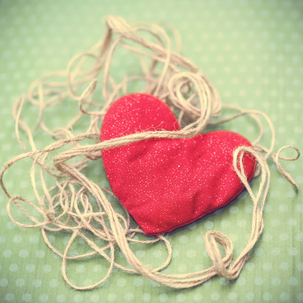 Красное сердце, завернутое в винтажную нить на зеленом фоне — стоковое фото