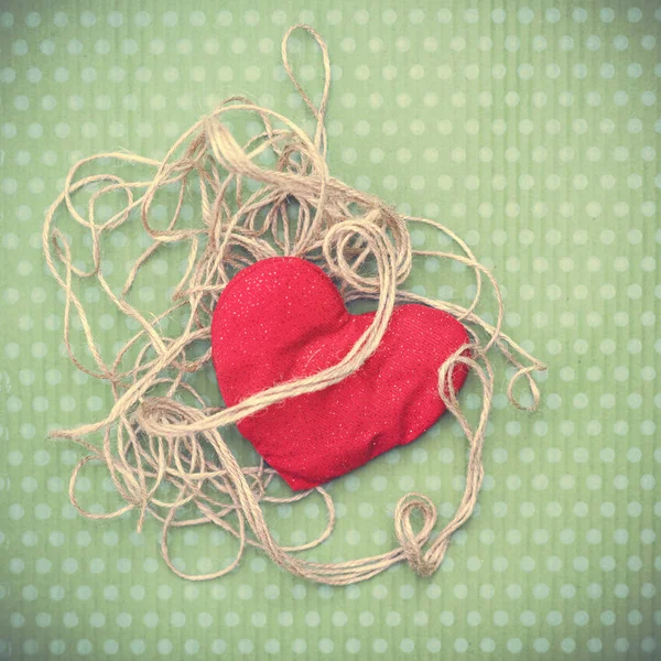 Coração vermelho envolto em fio vintage em fundo verde — Fotografia de Stock