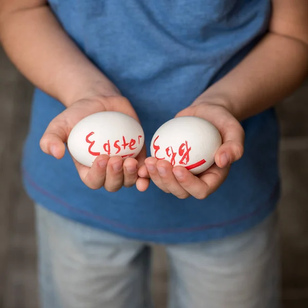 Eggs with the inscription Easter Egg in the hands of a child. Green background. Easter ideas. Space for text. Living Coral lettering. Happy easter.