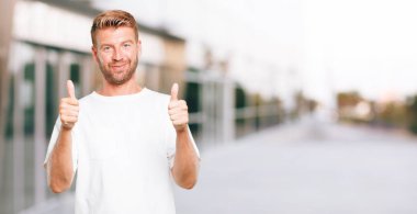 bir pozitif, gönderme Tamam tek eliyle sinyal genç sarışın adamla başparmak yukarıya, memnun, gururlu ve mutlu bir bakışla 