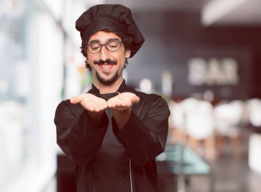 bir nesne veya kavramı her iki el ile gösterilen, ikisi de ileriye dönük memnun bir ifadeyle gülümseyen bir şef olarak genç deli adam.