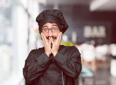 mutlu bir sürpriz ifade ile şef olarak genç deli adam, gözleri geniş açık ve geniş gülümseme, iki eliyle tutarak yüz.