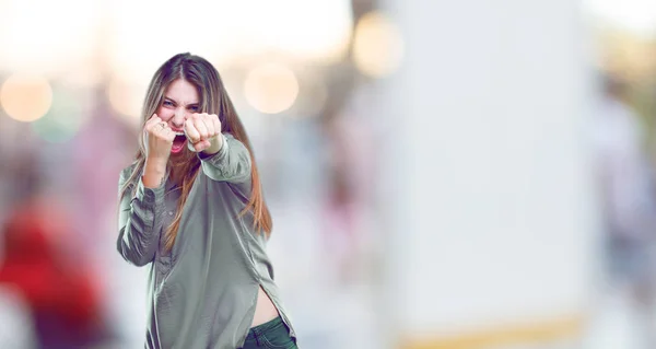 young beautiful girl with an angry, aggressive and menacing pose, ready for the fight, showing fists furiously and belligerently.