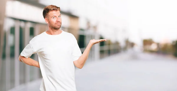 Joven Hombre Rubio Sonriendo Con Una Expresión Satisfecha Mostrando Objeto —  Fotos de Stock