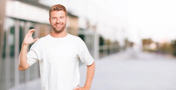 young blonde man smiling with a satisfied expression showing an object or concept which is held between both hands, in front.