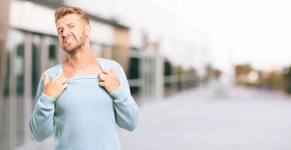 young blonde man with an anxious, stressed and nervous gesture, feeling under great pressure.