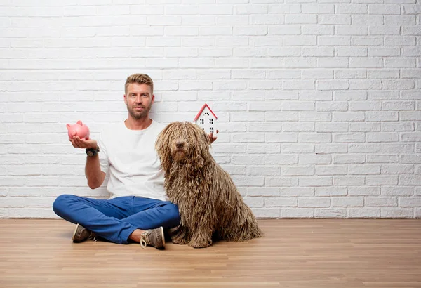 handsome blonde man with a dog, house model and a piggy bank