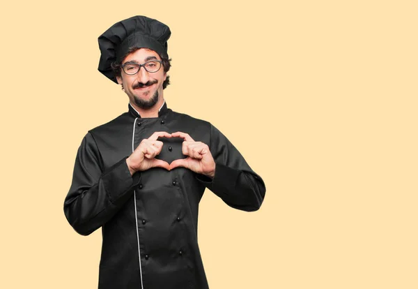 young crazy man as a chef smiling, looking happy and in love, making the shape of a heart with hands.