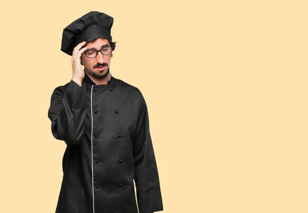 young crazy man as a chef looking stressed and frustrated, with closed eyes and hand on forehead.