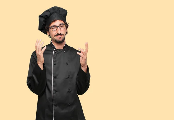 young crazy man as a chef looking stressed and frustrated, holding both hands open in front, expressing dismay and disbelief.