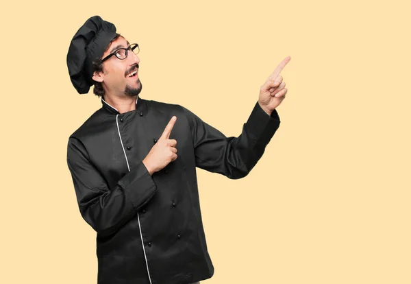 young crazy man as a chef smiling and pointing upwards with both hands, towards the place where the publicist may show a concept.
