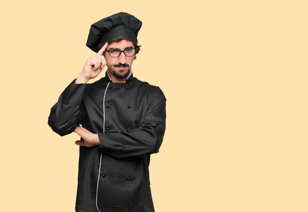 young crazy man as a chef Concentrating hard on an idea, with a serious far-off look, thinking with arm crossed in front and index finger pointing to forehead.
