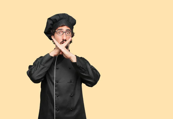 young crazy man as a chef with both hands crossed in front of mouth, in order to remain silent and keep a secret.