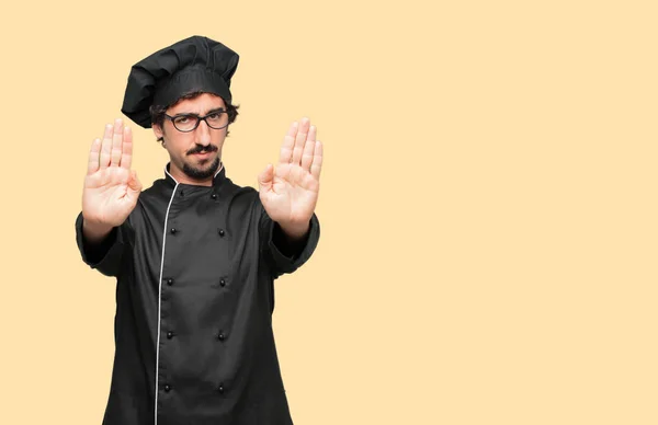 young crazy man as a chef Signaling stop with both palms of hands facing forward, with a serious and stern expression, forbidding.