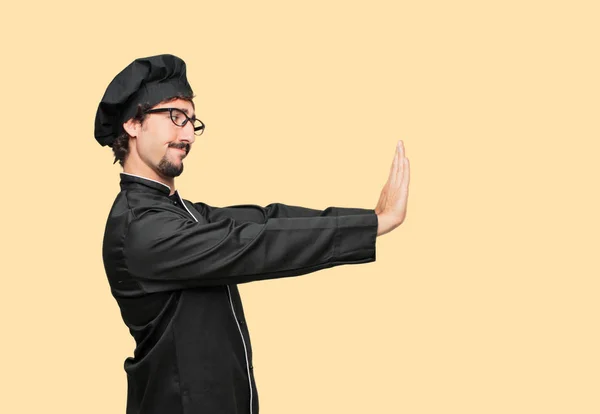 young crazy man as a chef signaling stop with both palms of hands facing forward, with a serious and stern expression, forbidding. Mid-lateral view.