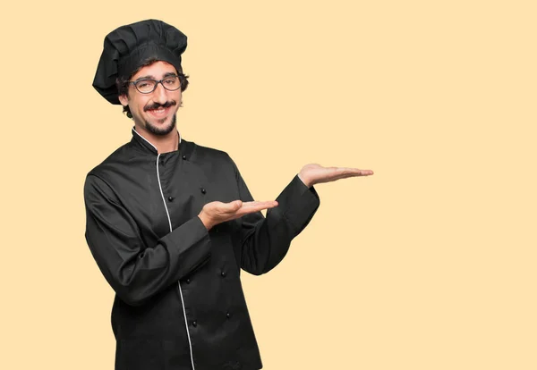 young crazy man as a chef smiling with a satisfied expression showing an object or concept with both hands.